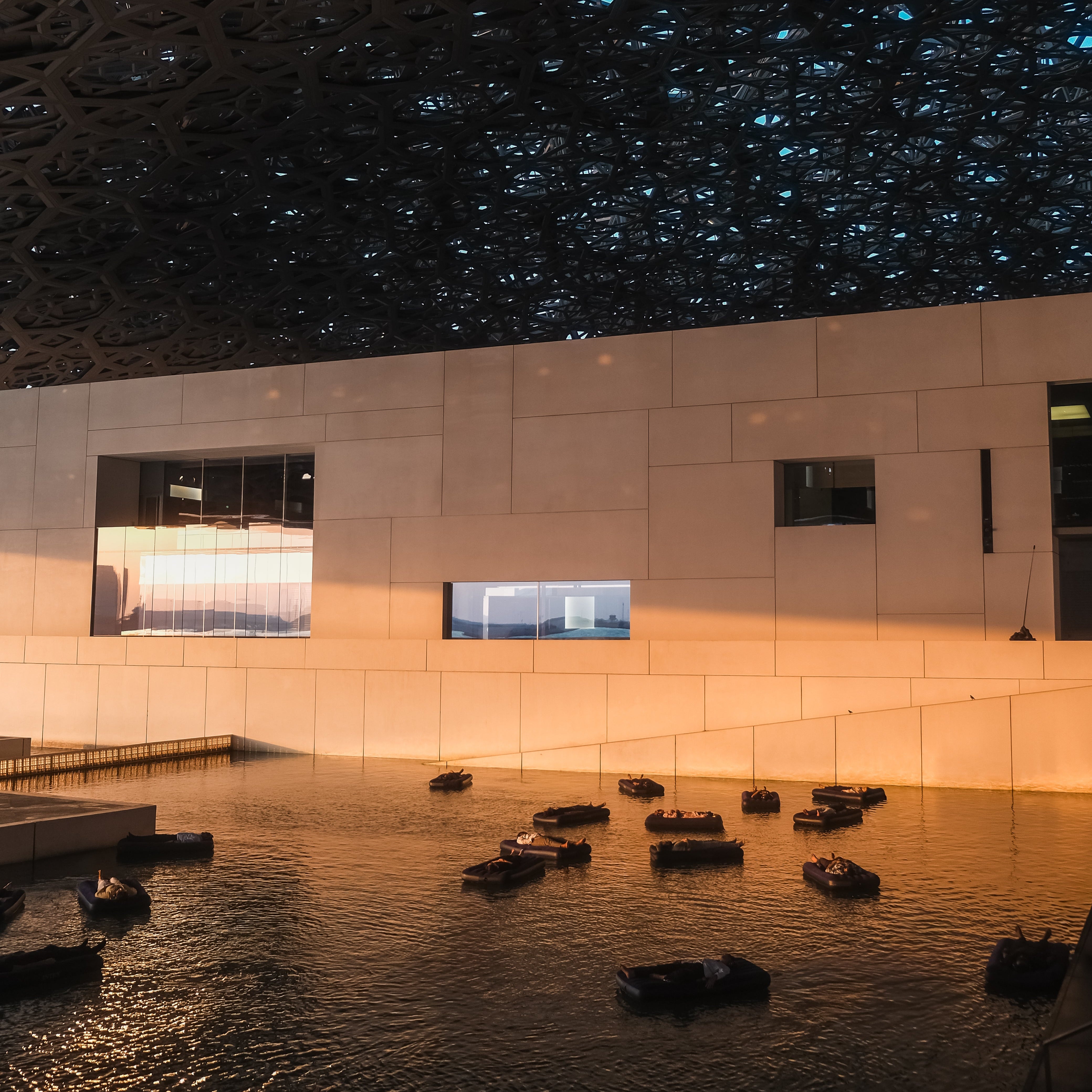 Louvre Abu Dhabi museum building with a water feature and intricate ceiling design at night.
